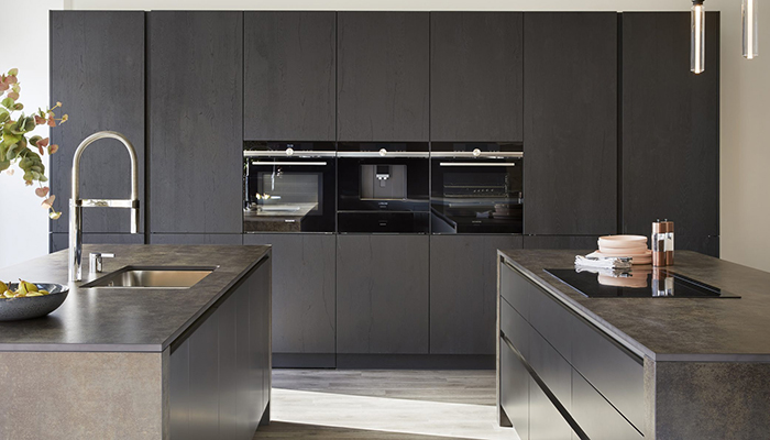 With Neolith's industrial collection worktop Iron Moss complete with bespoke waterfall edges, and units in dark ancient oak, this double island kitchen makes a statement in a design by Snug Kitchens