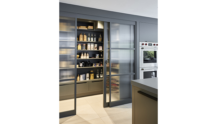 This glazed walk-in pantry, which features ribbed glass panels and a central sliding door, further enhances the expansive, ‘loft’ style ambience of an award-winning kitchen by Mowlem & Co. It features carefully custom-designed storage and is internally lit for maximum impact both inside and out