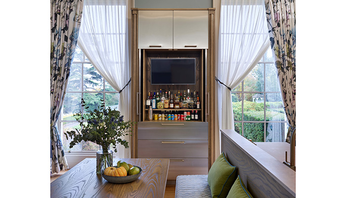This tall built-in bar cabinet is part of a bespoke stainless-steel kitchen with stained ash accents by Simon Taylor Furniture. Facing the dining area, and perfectly fitting between two tall windows, it features central pocket doors that open fully into recesses. There are two top boxes above and three deep drawers beneath to accommodate napkins and cocktail-making accessories
