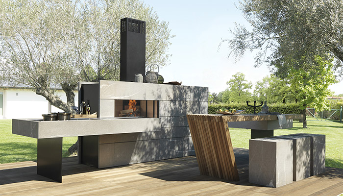 Modulnova’s new Outdoor Kitchen from DesignSpace London is built from solid Pietra Piasentina stone with a matt flamed finish, and made up of three architectural modules. The main block combines a wood-burning oven with storage and fronts which conceal both a fridge and an ice-maker. Set at a right angle, the floating worktop has an integral barbecue pit and a deep stone sink. It connects to the final element, a table constructed from solid Teak slats and set with Pietra Piasentina stone block stools