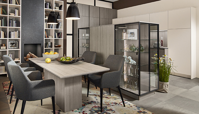 The versatile dining area in this Pronorm kitchen, featuring furniture from the Y-Line handleless and Proline ranges, can double-up as a home office during the day. The mid-height units in Vincenza Oak woodgrain are perfect for tidying work items away when not required while the back-to-back glass display cabinets act as a room divider 