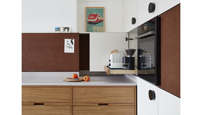 Handcrafted stained oak cabinetry is paired with a stained cork backsplash in this award-winning Seaside Kitchen design from H. Miller Bros, which shows how integrated handles can elevate a simple design