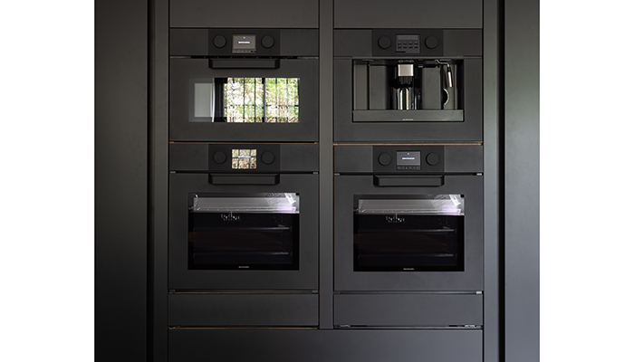 Handleless Neil Norton Design furniture featuring matt black Icon Exclusive appliances with black rubber dials, including a combination microwave, coffee machine, two ovens, warming drawer and vacuum sealer drawer