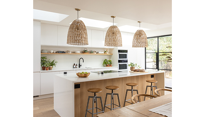 Wooden accents inject natural warm tones and a sense of textural tranquility in this contemporary Pure white kitchen by John Lewis of Hungerford. The eye-catching fluted finish on the island links beautifully with the wicker pendants from Nkuku, which are suspended above to create a relaxed yet sophisticated design 