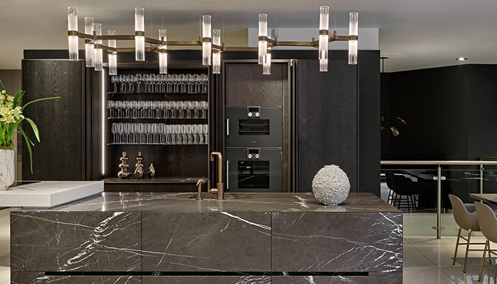 The burnished brass finish of Empty State’s Branch pendant, which features 13 illuminated glass tubes, was chosen by Halcyon for its warmth and to blend seamlessly with the other metals, such as the tap, used in this dark and dramatic Eggersmann kitchen