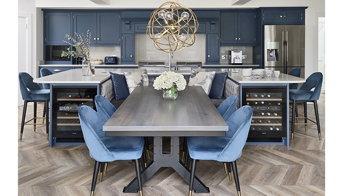 This bespoke Shaker kitchen by Simon Taylor Furniture includes a U-shaped island with a central banquette upholstered in grey velvet. Four additional chairs provide space for a total of six diners to sit comfortably around the industrial-style table