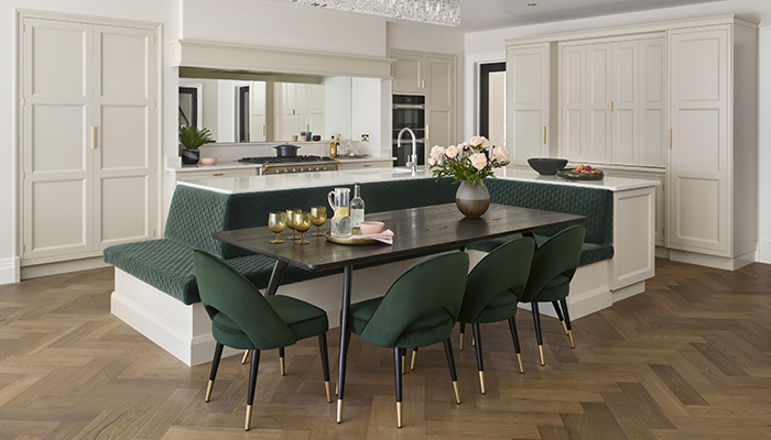 The bench seating, which is upholstered in vibrant green velvet fabric, follows the contours of the L-shaped island to take centre stage in this Martin Moore kitchen featuring the New Deco collection painted in Grey Moonstone. For added flexibility, the dining table and chairs can be removed as required