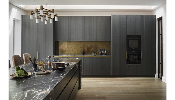 A bespoke kitchen by Roundhouse is showcased in bookmatched veneer with antique brass accents and African fusion quartzite worktops, creating a look that is dark and dramatic without overwhelming the space