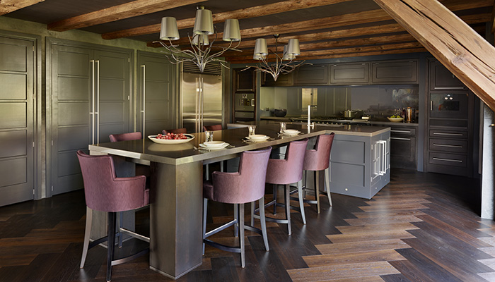 The bespoke cabinetry shown here takes its inspiration from Martin Moore’s Architectural Collection, featuring clean lines and minimal detailing. It is hand painted in a bespoke dark grey-blue from Martin Moore, while the ‘cooking capsule’ at the far end of the room has a contemporary, letter box design in a natural oak finished with a bespoke dark stain. A tall table with solid block legs and a large composite top forms the central, social feature