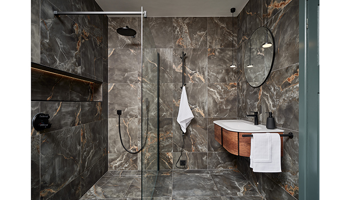 This dark and dramatic ‘his’ en suite was created by Ripples and features smoky grey onyx-effect tiles, matt black brassware and a rust oak curved vanity unit with mineral cast washbasin. The fully-tanked wetroom provides easy access showering while the illuminated wall niche offers additional storage