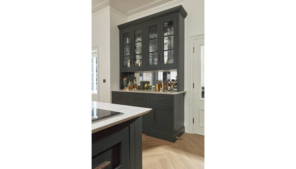 A hotel-style drinks station designed by Tom Howley from the Kavanagh Collection in avocado with mirrored back panel and overhead display cabinets for a statement piece in a larger kitchen layout