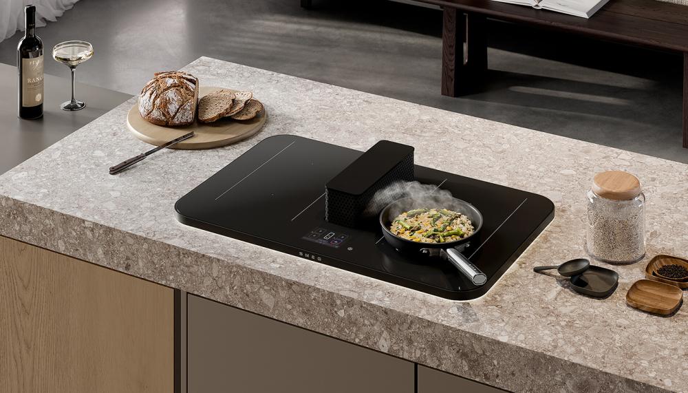 The Smeg Isola ALTA PRO is a premium 83cm induction hob featuring a motorised, elevating central downdraft extractor, designed with Stefano Boeri Interiors for high-end kitchens. With a 5-inch Vivoscreen touchscreen, FollowPot technology, and matt black scratch resistant surface