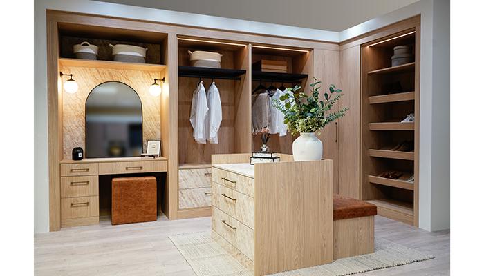 This dressing-room scheme by Daval Furniture uses its Lugano collection in New England Oak paired with drawer fronts in Finsbury Tan Marble. It features a central island with upholstered seating and drawer unit, a shoe wardrobe, open hanging sections, and an integrated dressing table