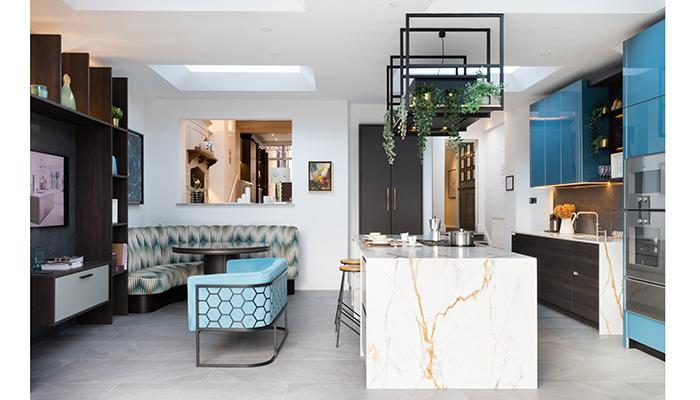 The new open plan Garden Room extension features gloss glass and dark oak grain-matched furniture by EWE, a Dekton cladded waterfall island with Vario 400 cooking appliances by Gaggenau. A Novy Pureline Frame recirculation extractor is suspended above. The space includes a dining area with curved banquette; a media area used for client presentations and a floor-to-ceiling bar area