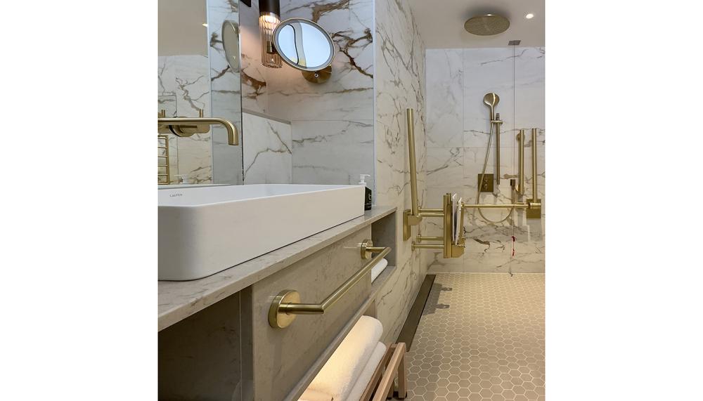 Designed to be inclusive and effortlessly elegant, this bathroom at the Montcalm Mayfair hotel in London features grab rails, back rests and white pad shower seats finished in PVD Satin Brass from Fitzroy of London&rsquo;s Gosfield collection