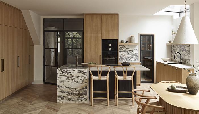 This luxurious kitchen features a bold marble worktop with waterfall edge and dark, ribbed panelling on the underside of the island, which contrasts with the natural oak veneer cabinetry